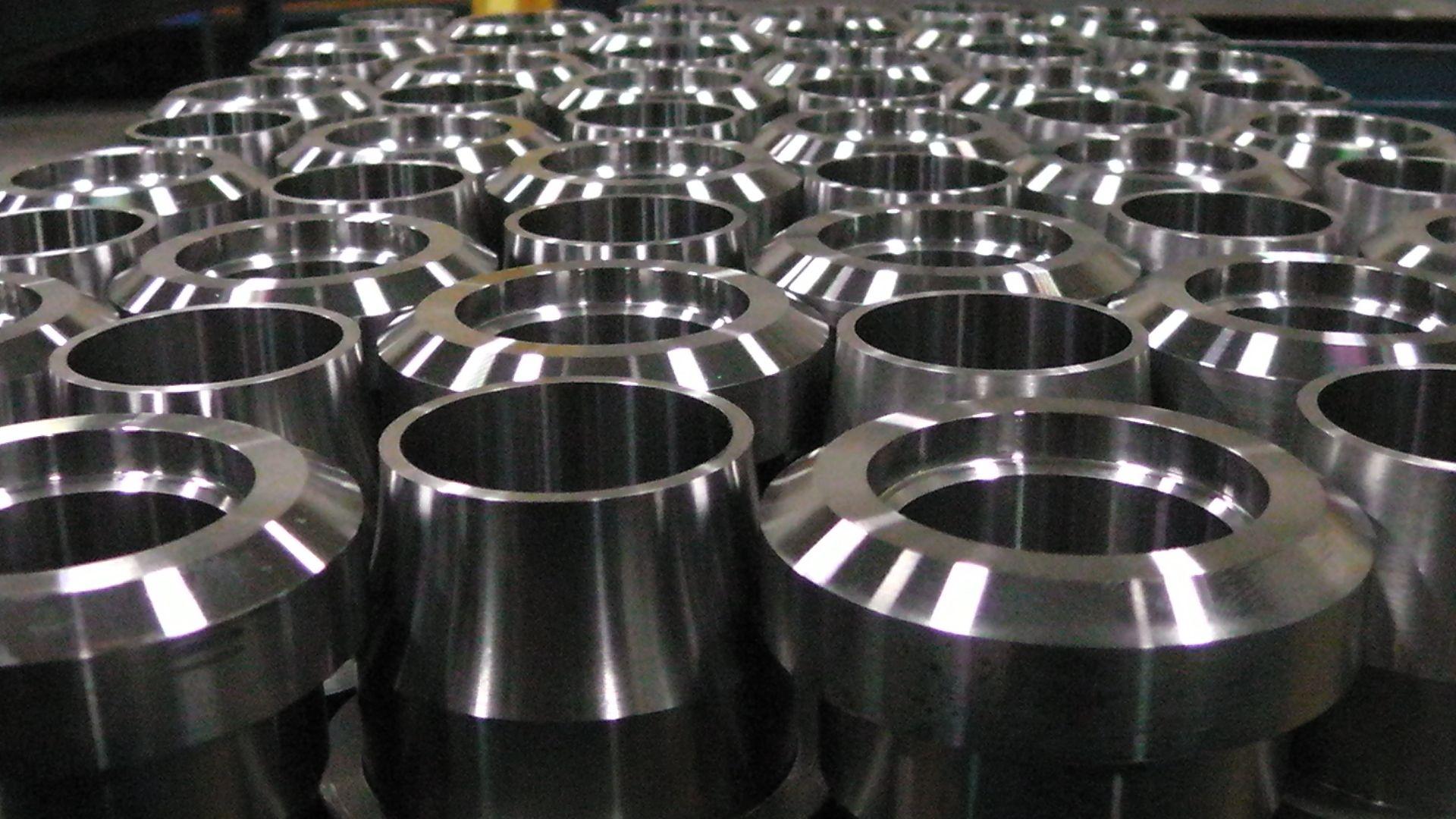 De nombreuses pièces cylindriques métalliques usinées identiques, disposées en grille sur une surface plane.