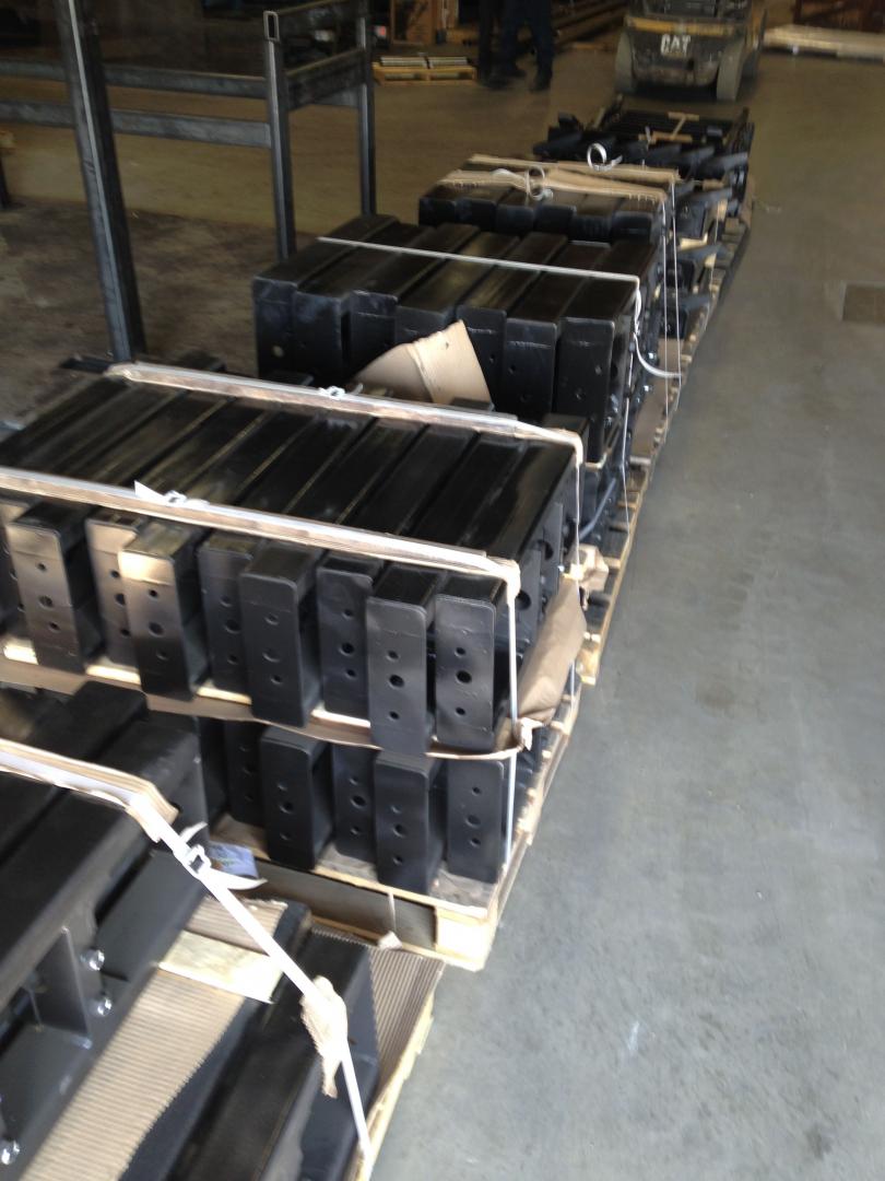 A warehouse pallet loaded with stacked, rectangular black metal components secured by straps.