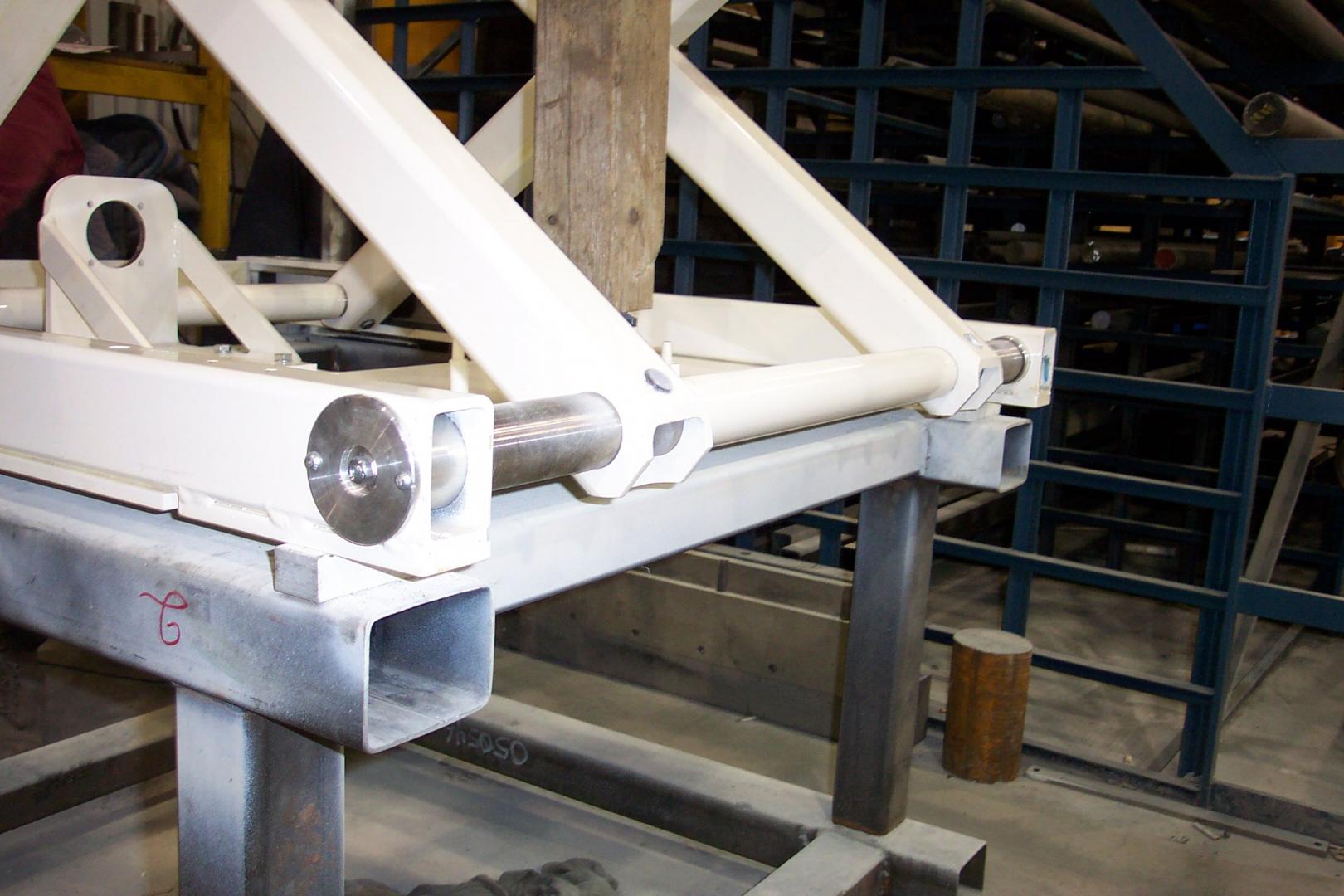 A white metal scissor lift mechanism is mounted on a gray steel frame in an industrial workshop.