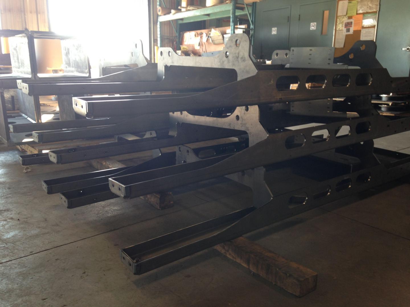 Several large, dark metal industrial frames are stacked horizontally on wooden blocks in a manufacturing workshop.