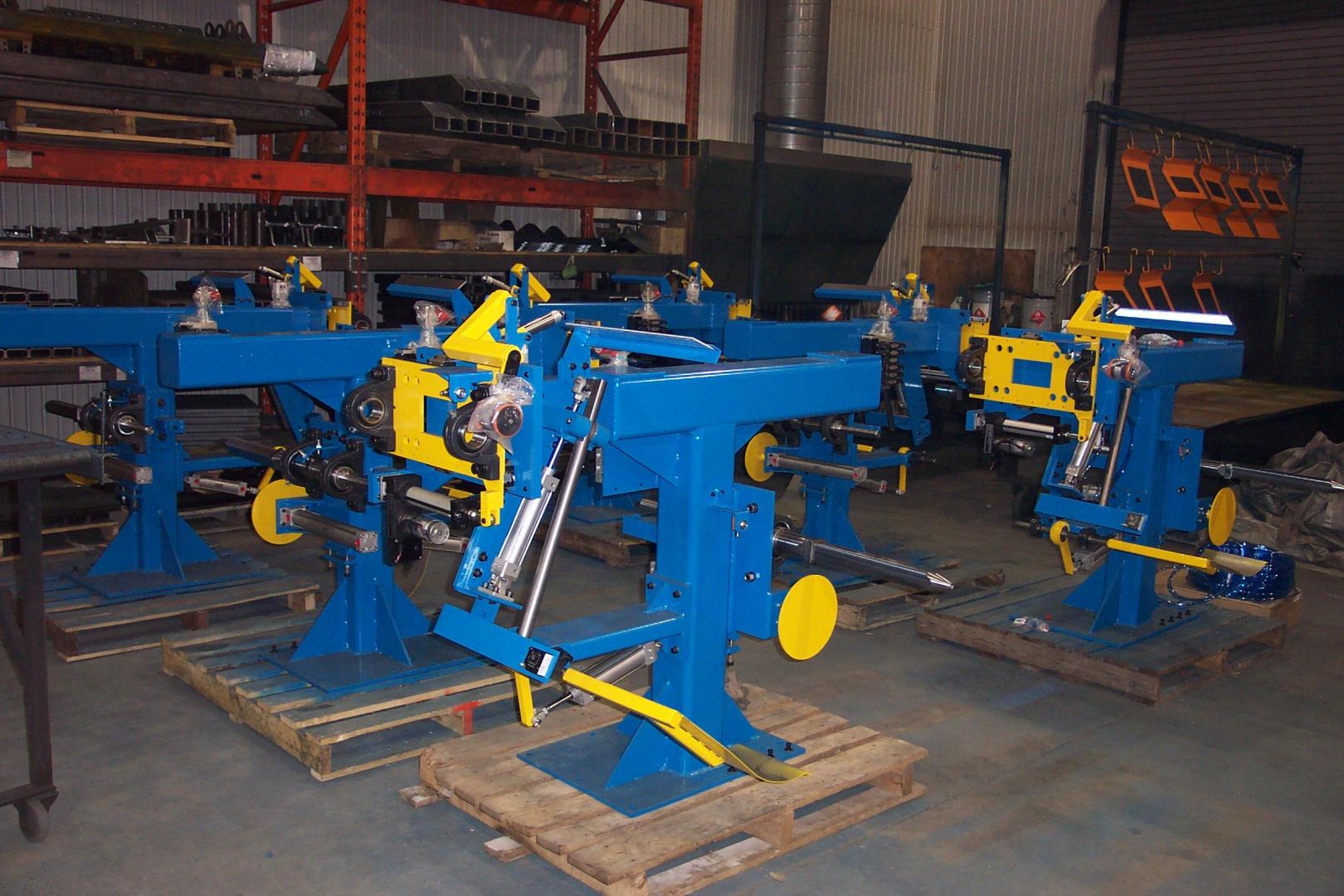 Several bright blue industrial machines with yellow accents sit on wooden pallets in a warehouse.