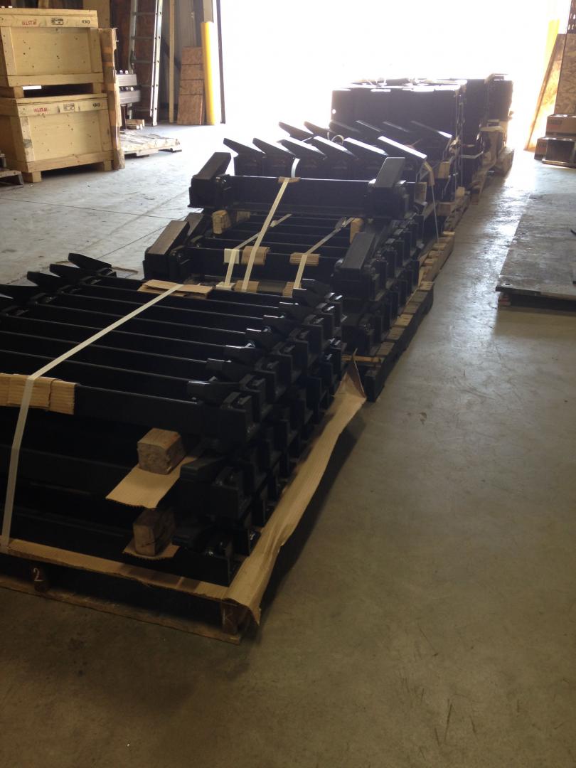 A wooden pallet stacked with long, black metal industrial parts, secured with plastic straps in a warehouse setting.