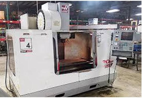 A white Haas VF-4 vertical machining center sits on a factory floor with a control panel extended to the right.
