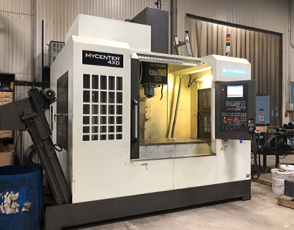 Une fraiseuse CNC Kitamura Mycenter 4XD blanche est installée dans un atelier dont la porte et le panneau de commande sont ouverts.