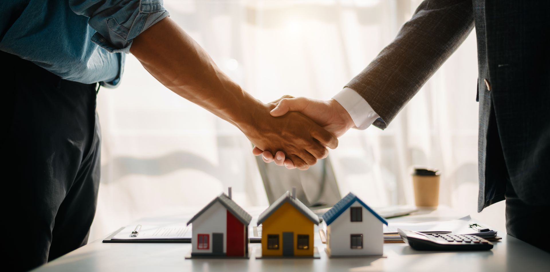 Two men are shaking hands over a table with small houses.