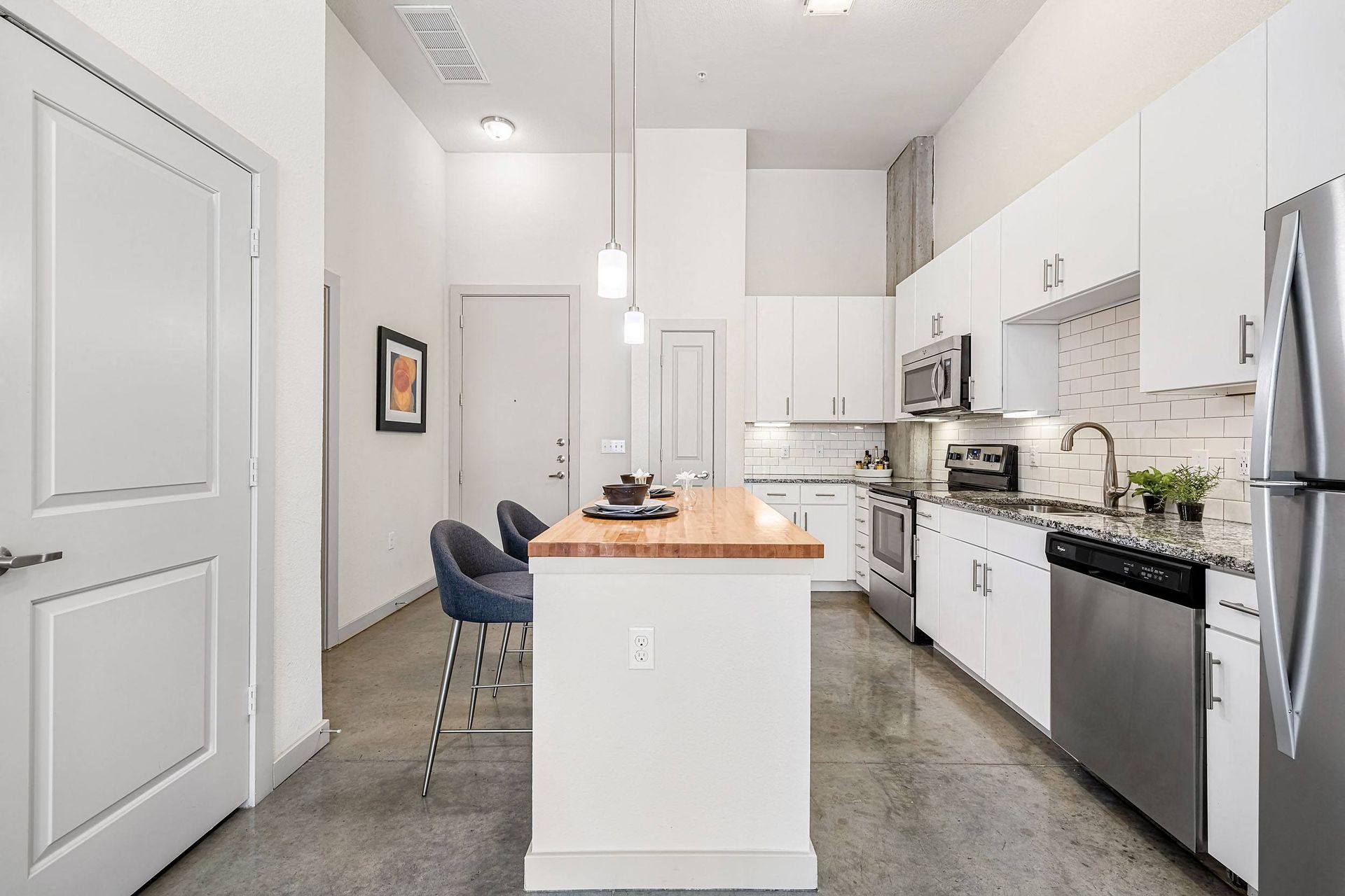 Bright modern kitchen with white cabinets, island, stainless appliances, and two blue chairs at Marq on Burnet