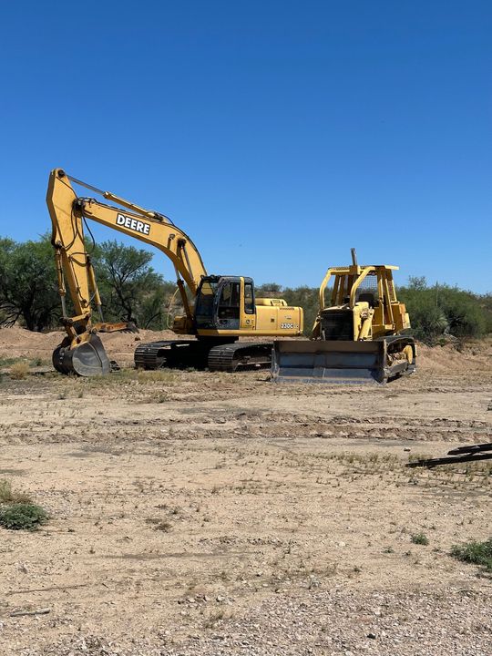 Yellow excavator and bulldozer on a dirt lot under a clear blue sky