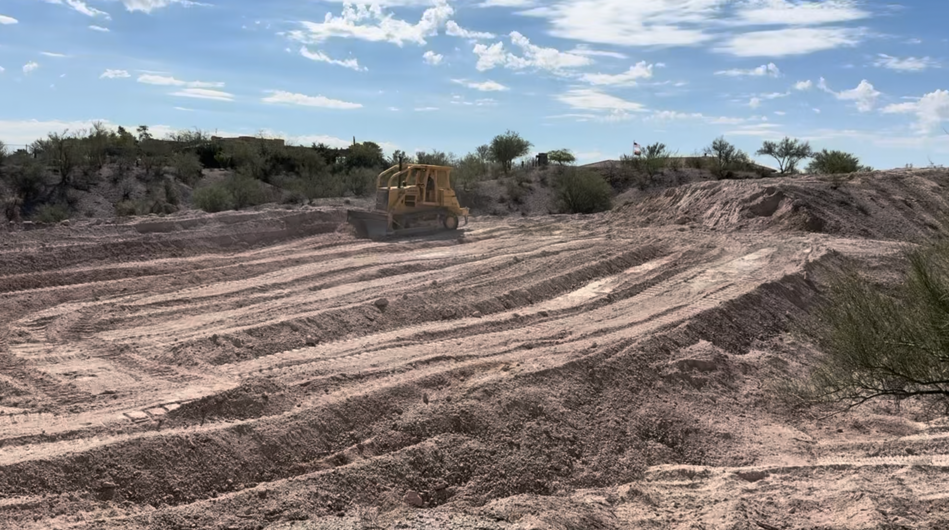 Bulldozer grading a dirt lot with tire tracks under a blue sky