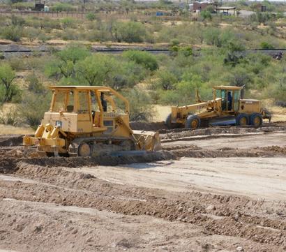 Two yellow bulldozers working on a dirt road in a dry, scrubby landscape