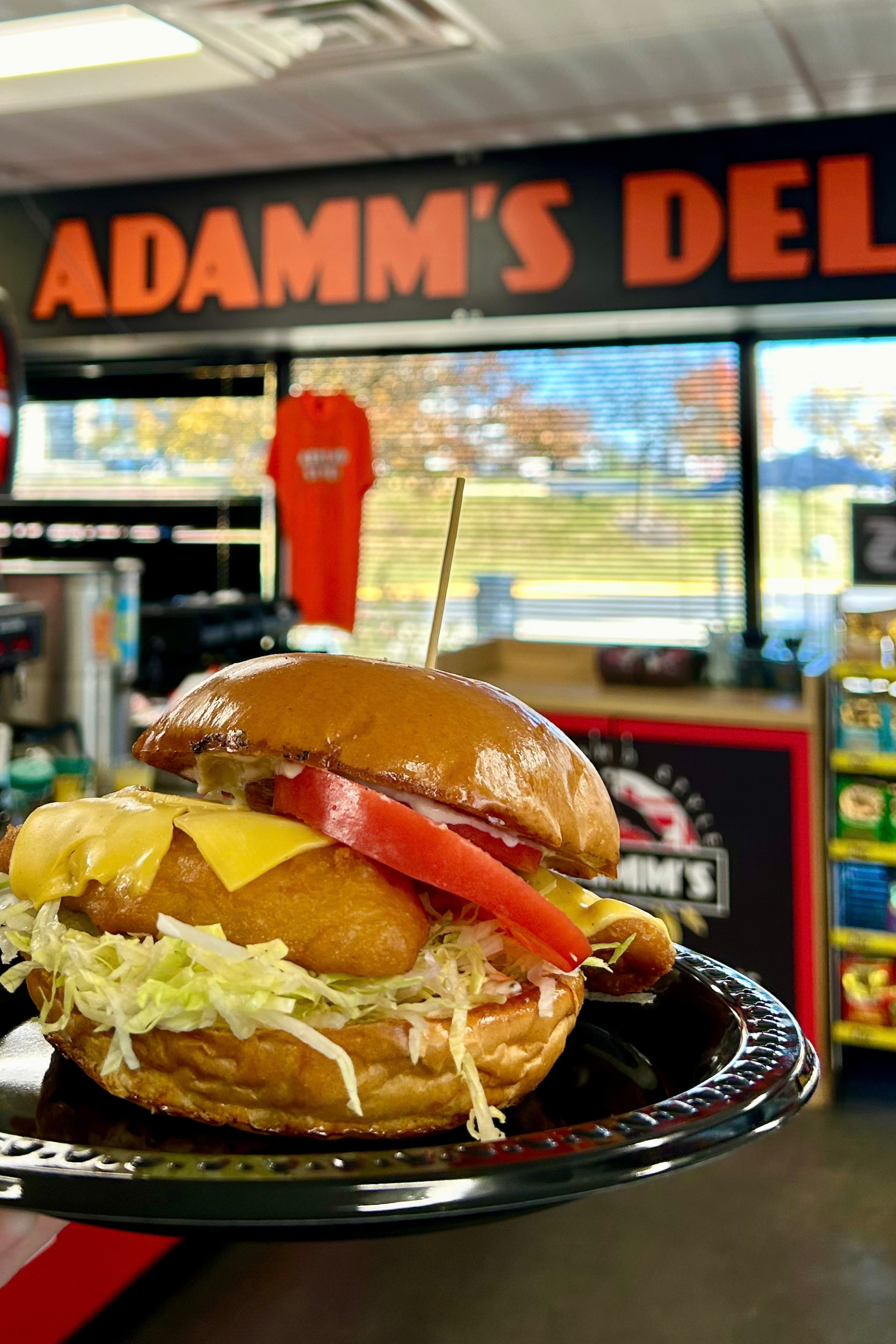 Adamm's Deli breaded chicken on a plate in a deli, with lettuce, tomato, and in front of a counter.