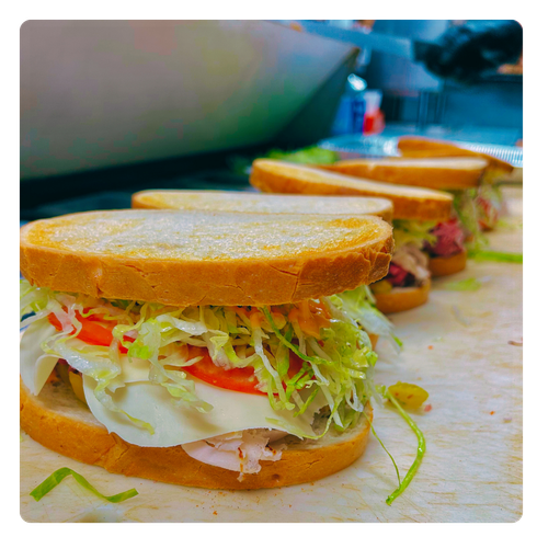 Three deli sandwiches on a counter, stacked with lettuce, tomato, and cold cuts