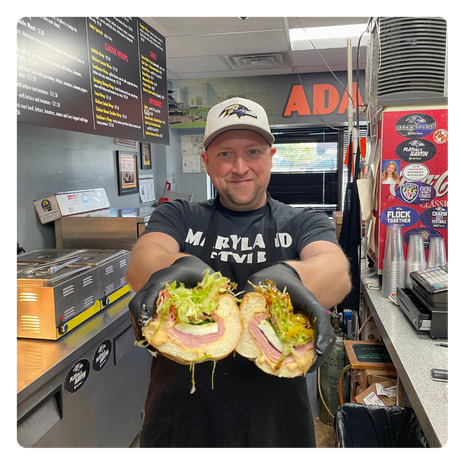 Owner Adamm Houck holding cold cut subs in both hands