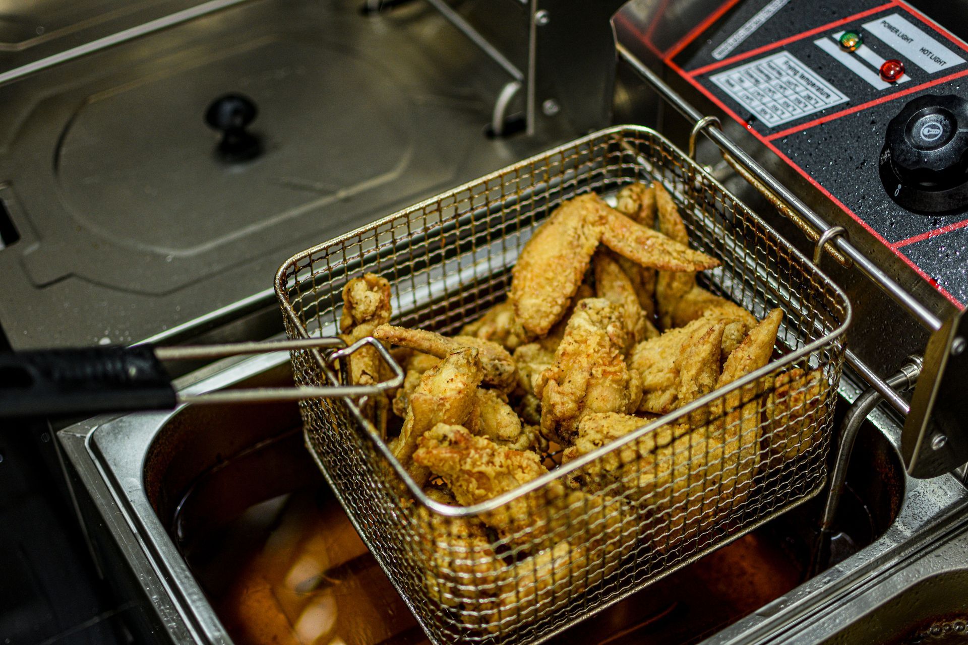 Golden fried chicken pieces in a metal fryer basket draining oil inside a commercial kitchen
