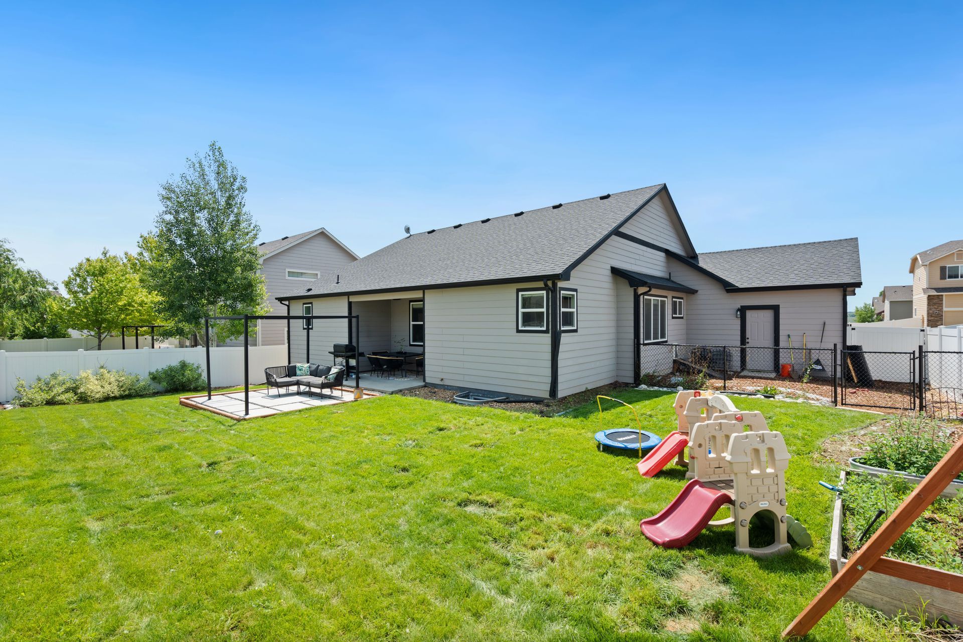 Backyard view of suburban single family home with a playground and trampoline for toddlers and a patio.