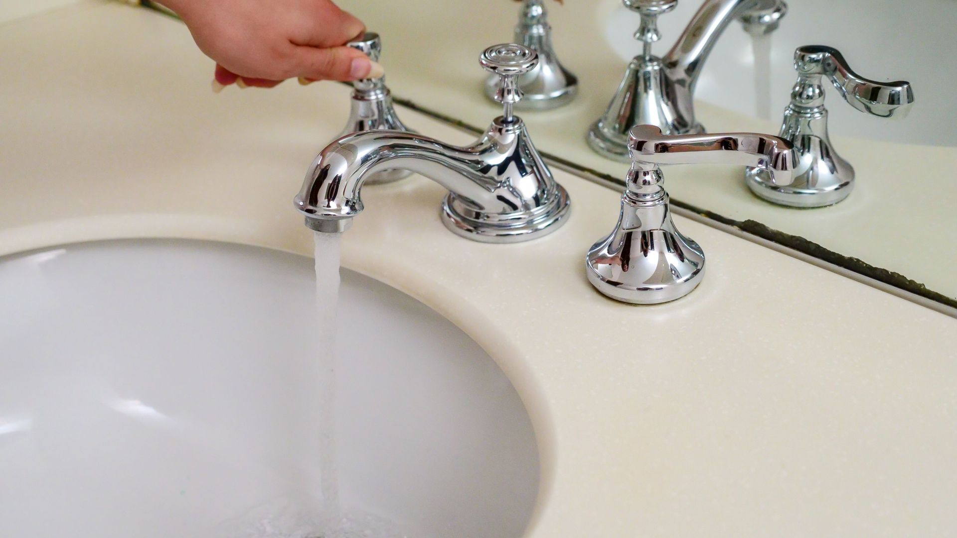 Person turning on the hot water side of a silver, bathroom hand sink.