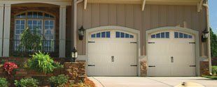 Suburban house front with two beige garage doors, arched windows, and a brick entry walkway