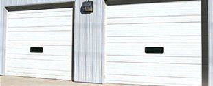 Two white garage doors with a central gray divider in a building exterior