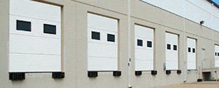 Row of white loading dock doors with small windows on a beige warehouse wall