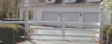 White wooden gate across a driveway in front of a house, with trimmed hedges on both sides