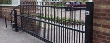 Black metal gate beside a brick wall, blocking a walkway by a street