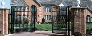 Open black gates at the entrance to a brick apartment complex with a green lawn and sidewalk