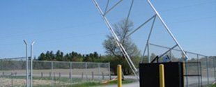 Fenced utility site with a large tilted satellite dish under a blue sky