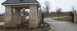 Stone gate entrance with a closed wrought-iron driveway gate on a rainy day