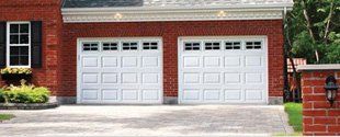 Red brick house with two white garage doors and a driveway in front