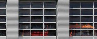 Side view of a fire station with garage doors and a red emergency vehicle inside one bay