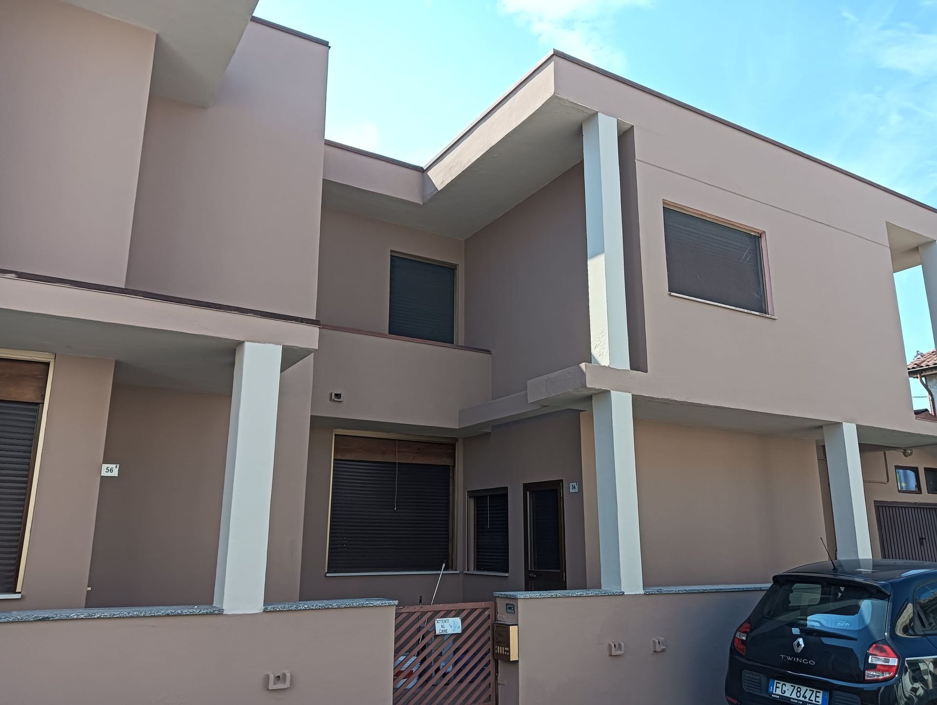 Casa moderna a due piani di colore beige con cancello d'ingresso e un'auto nera parcheggiata nel vialetto.
