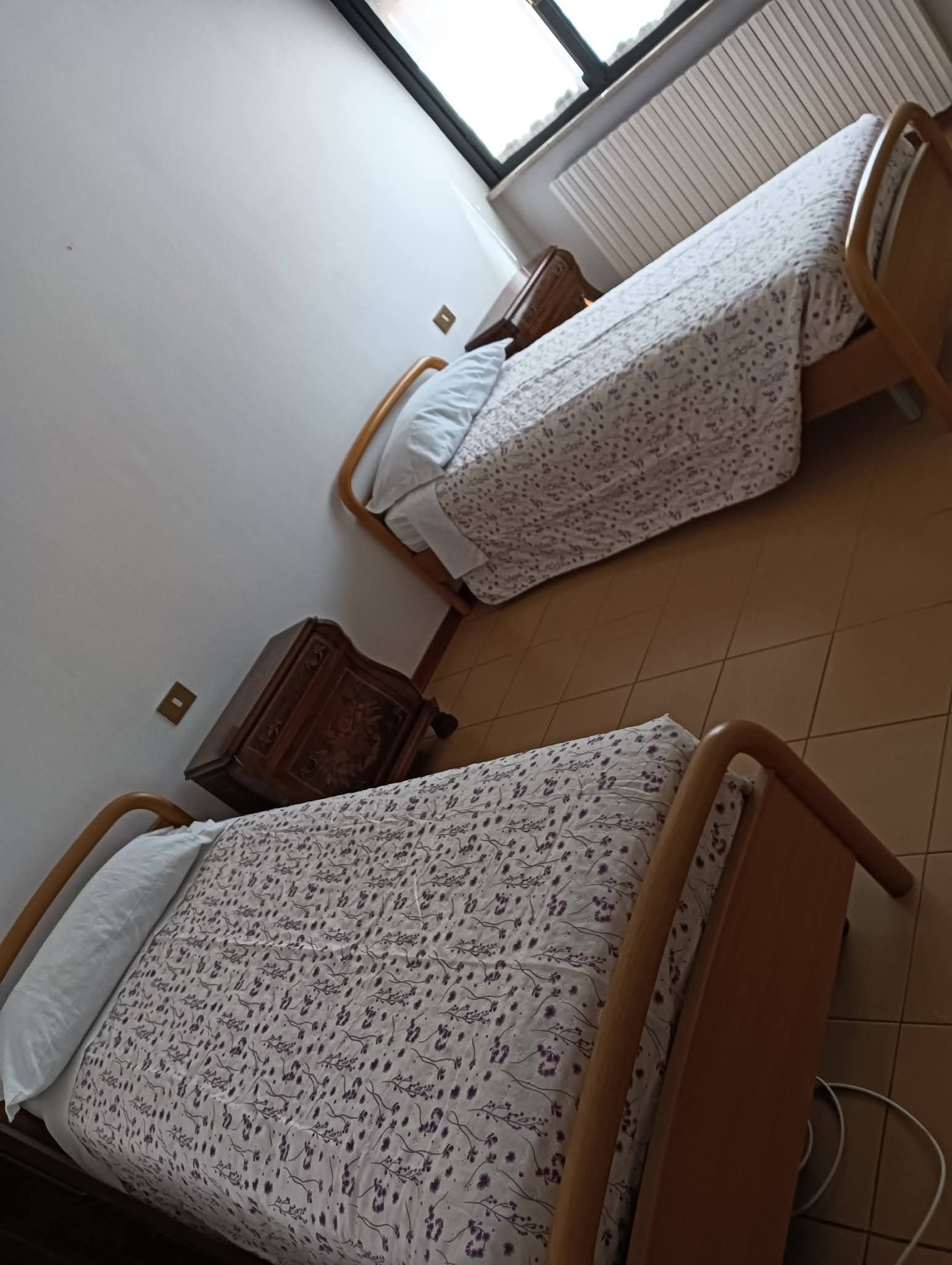 Piccola camera da letto con due letti singoli, biancheria da letto a fantasia e una finestra con tende.