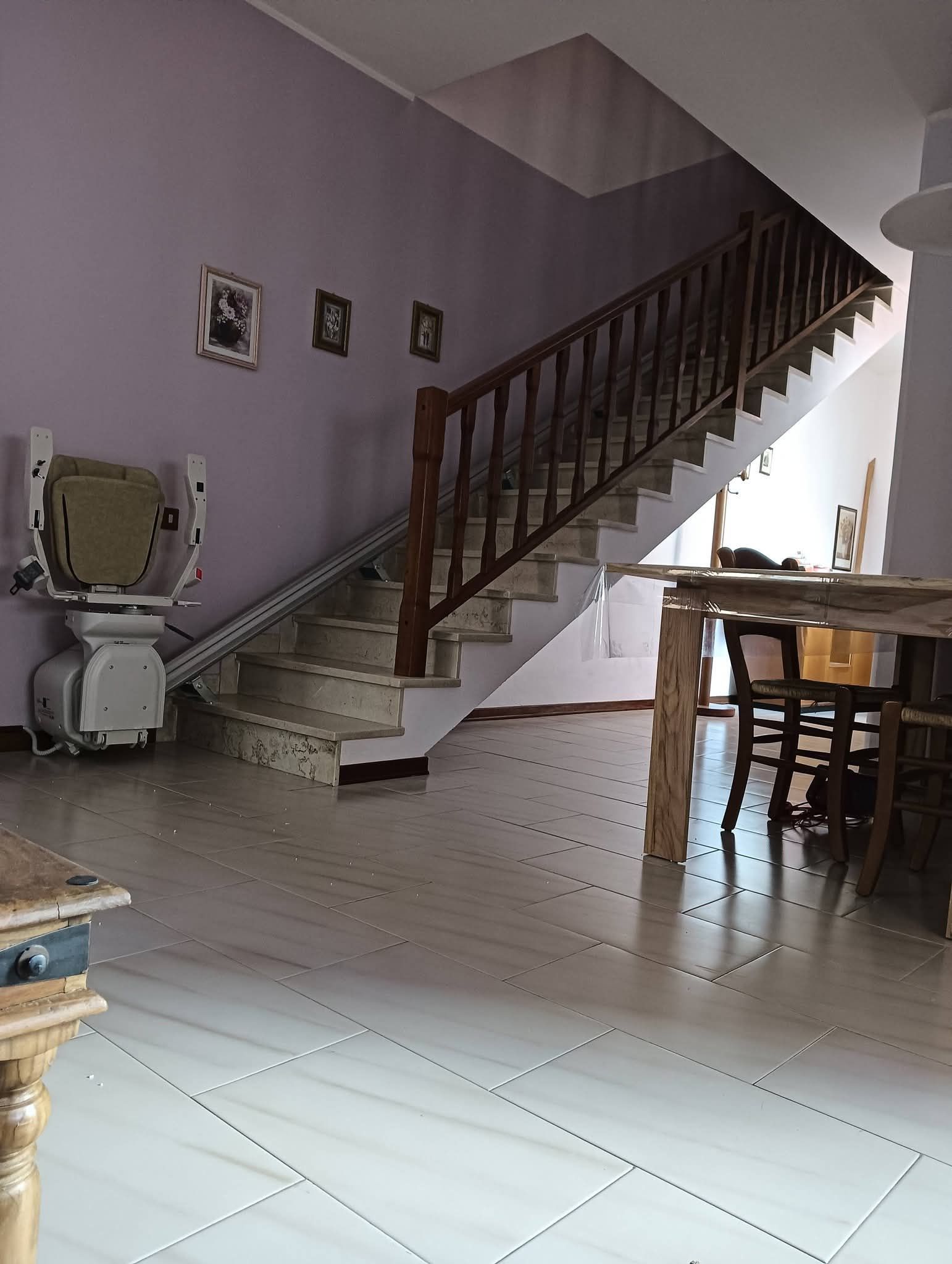 Scala in una casa con pareti viola, pavimento in piastrelle bianche e tavolo da pranzo vicino a una finestra luminosa.