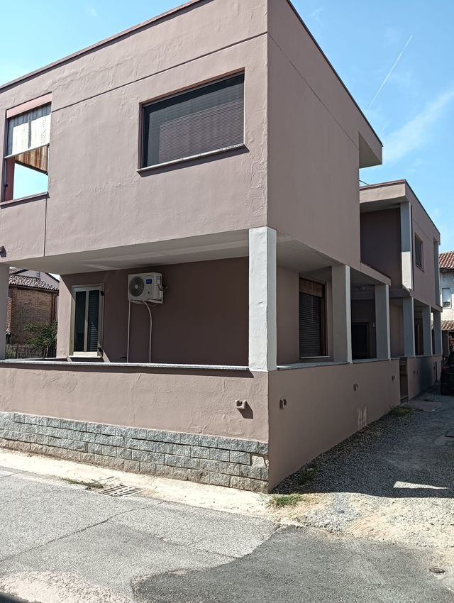 Casa beige a due piani con basamento in pietra, balcone anteriore e vialetto stretto sotto un cielo limpido