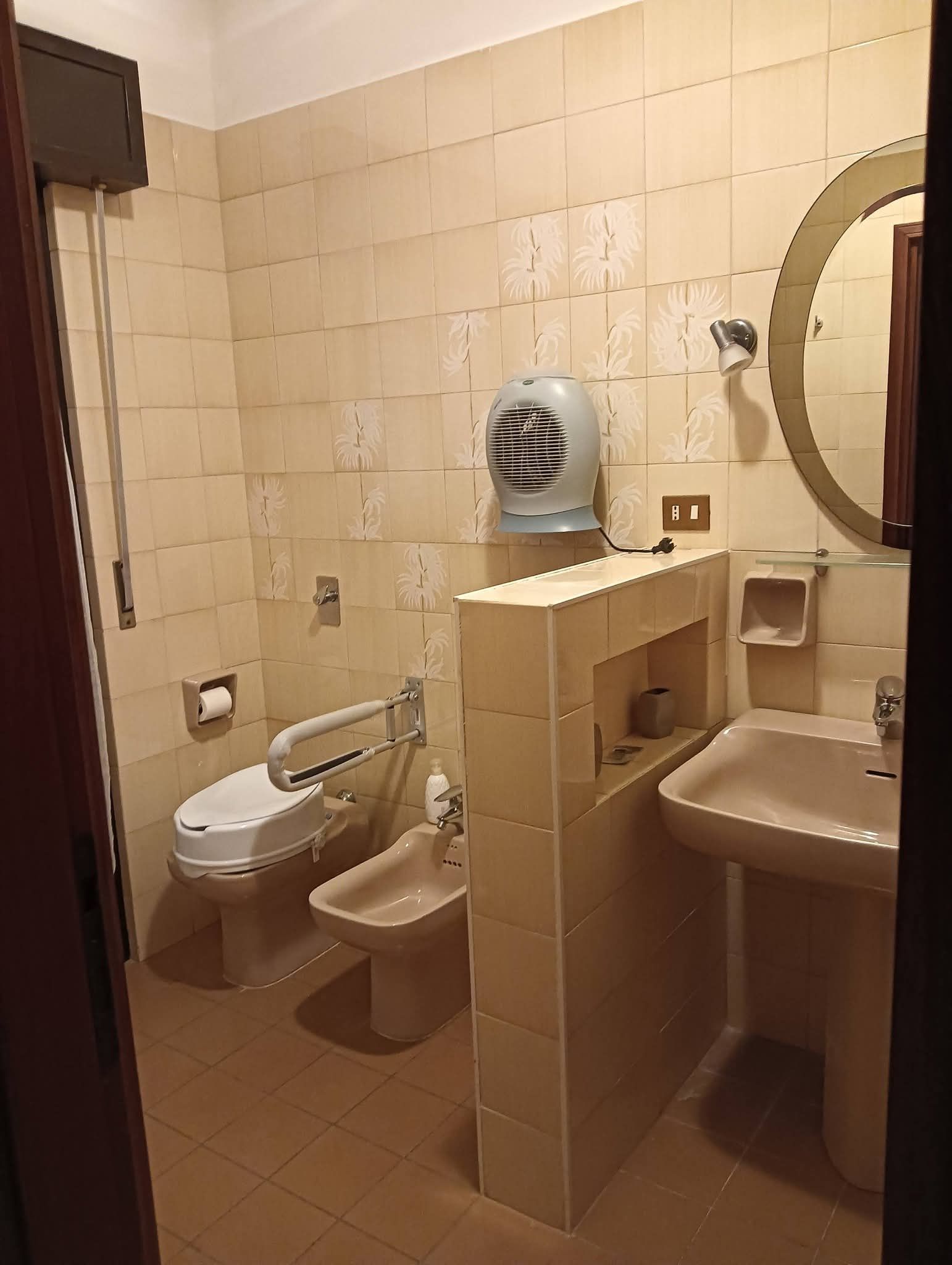Piccolo bagno piastrellato di beige con WC, lavandino, specchio e vasca da bagno a vista.