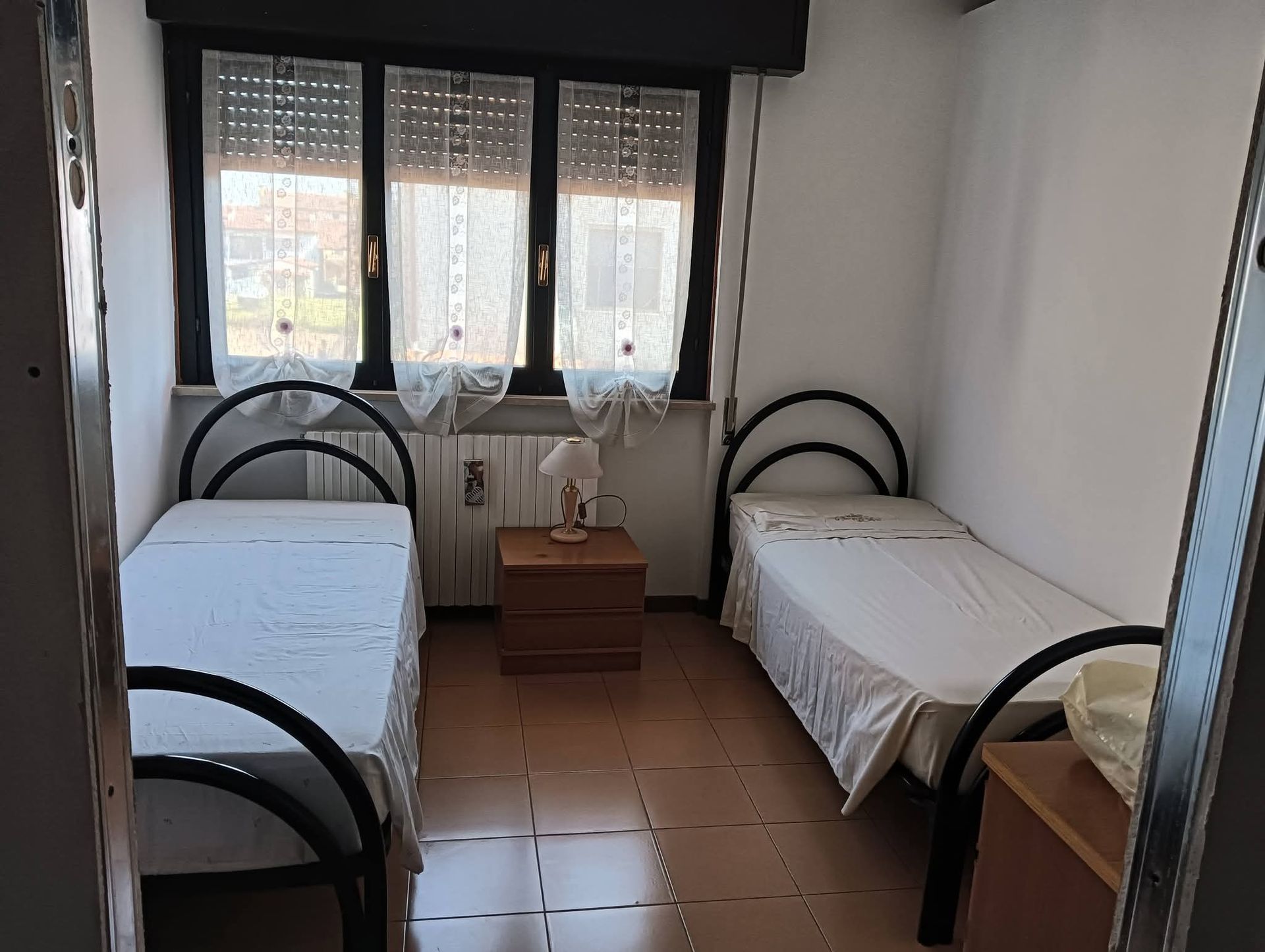Piccola camera da letto con due letti singoli, una finestra e un comodino tra di essi.