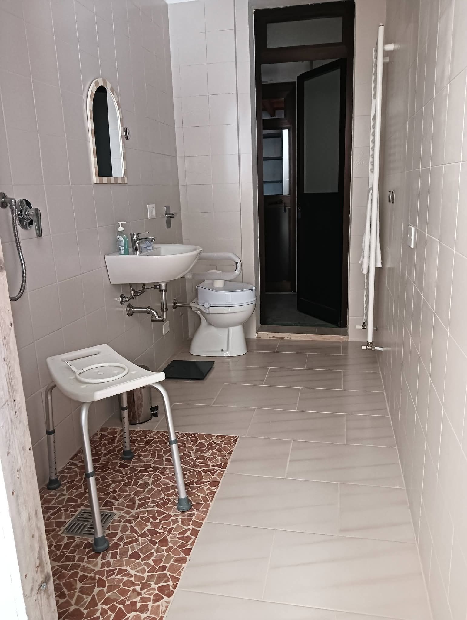 Bagno stretto piastrellato con lavabo, WC, specchio e piccolo sgabello su un pavimento a mosaico.