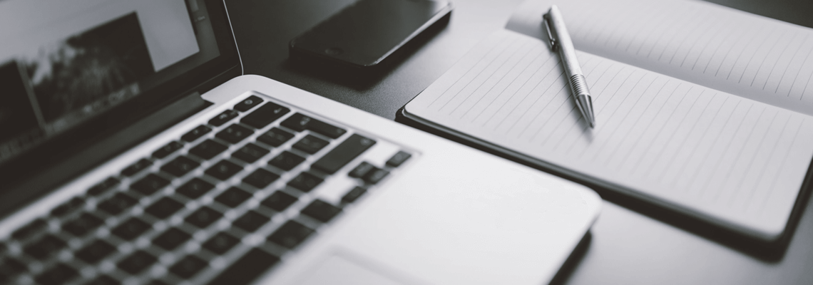 a pen is lying on a notebook next to a laptop and a phone