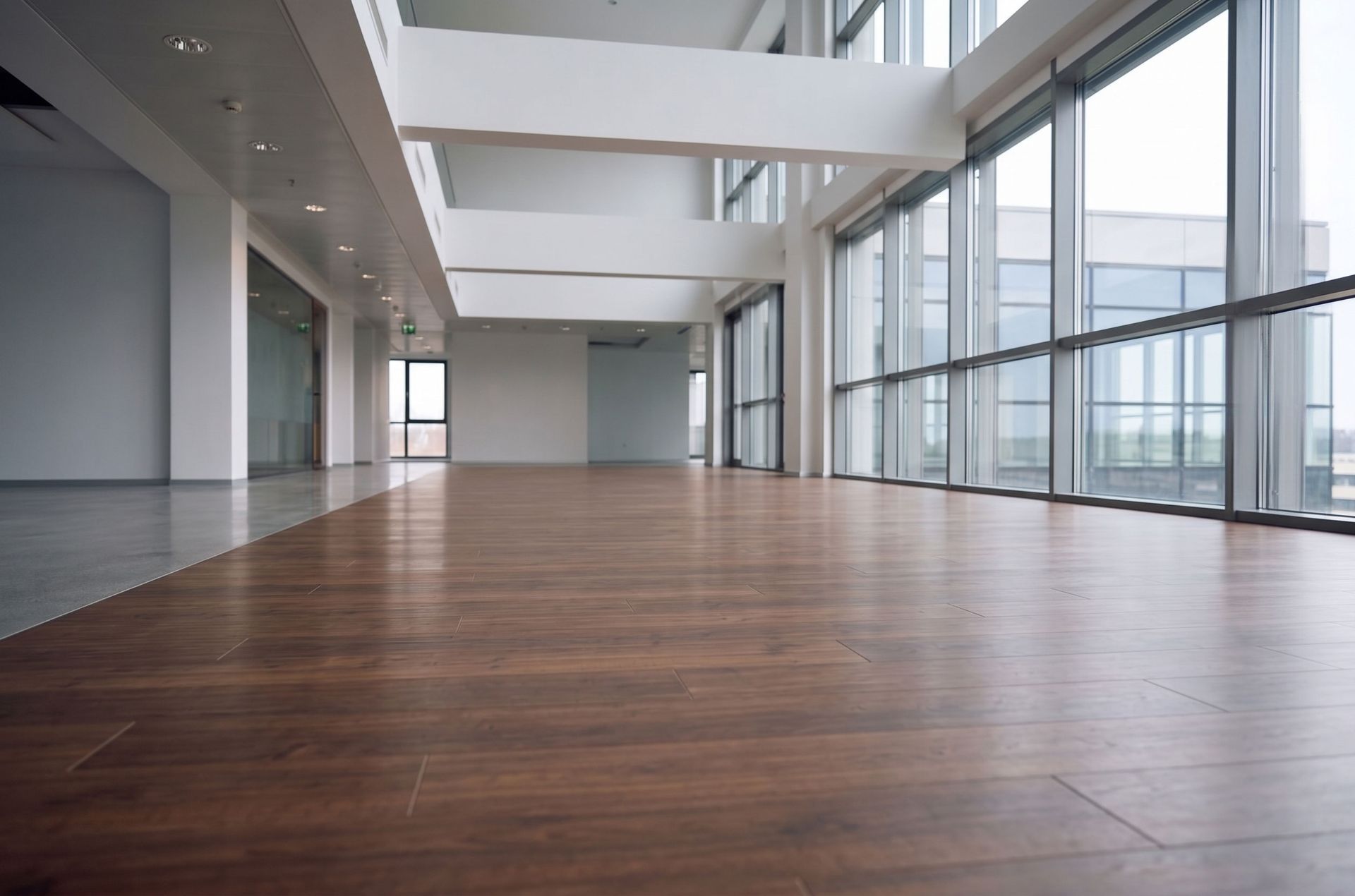 Empty modern office with wood floor, large windows, and white walls