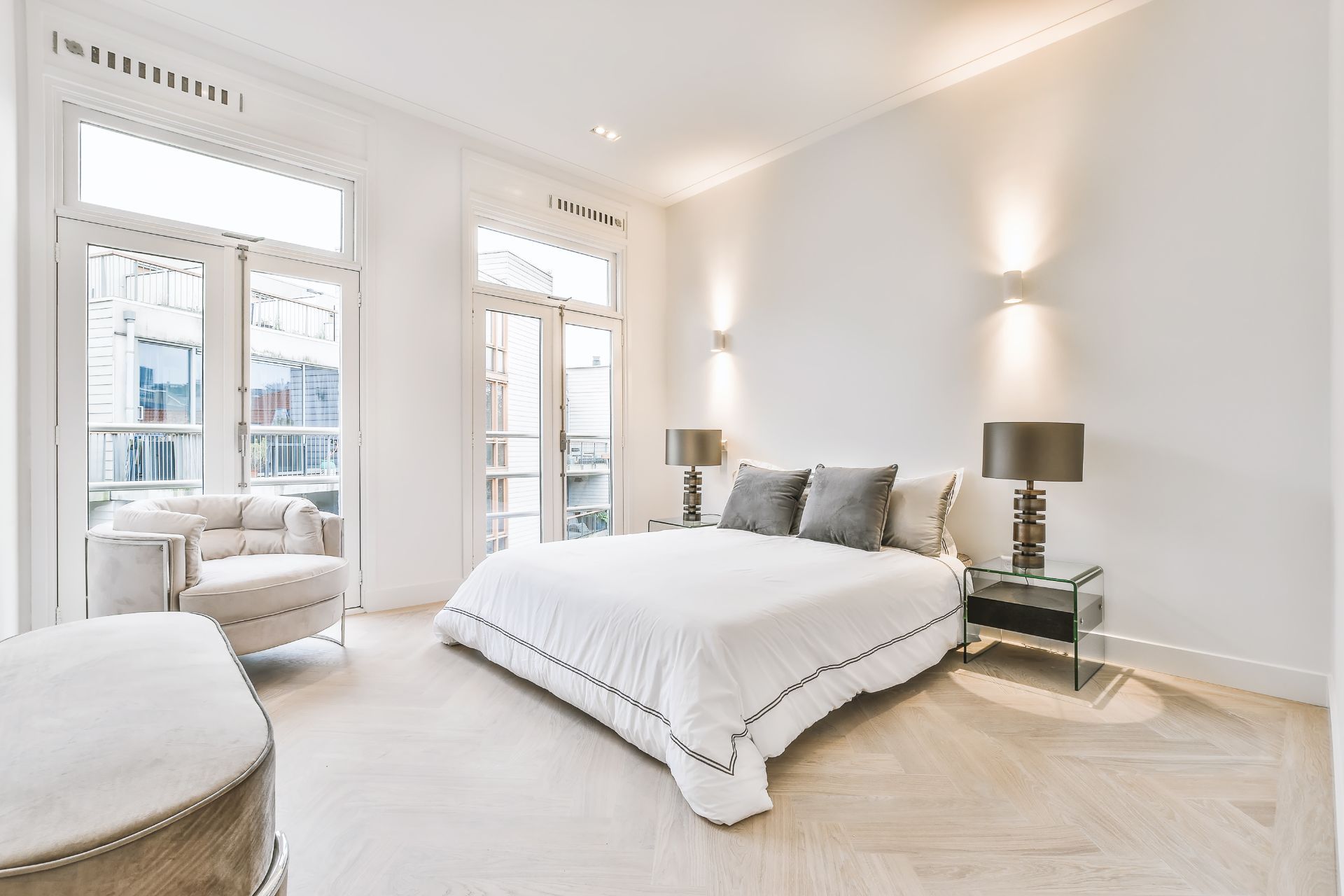 Bright minimalist bedroom with a large bed, white walls, tall windows, and mirrored bedside tables