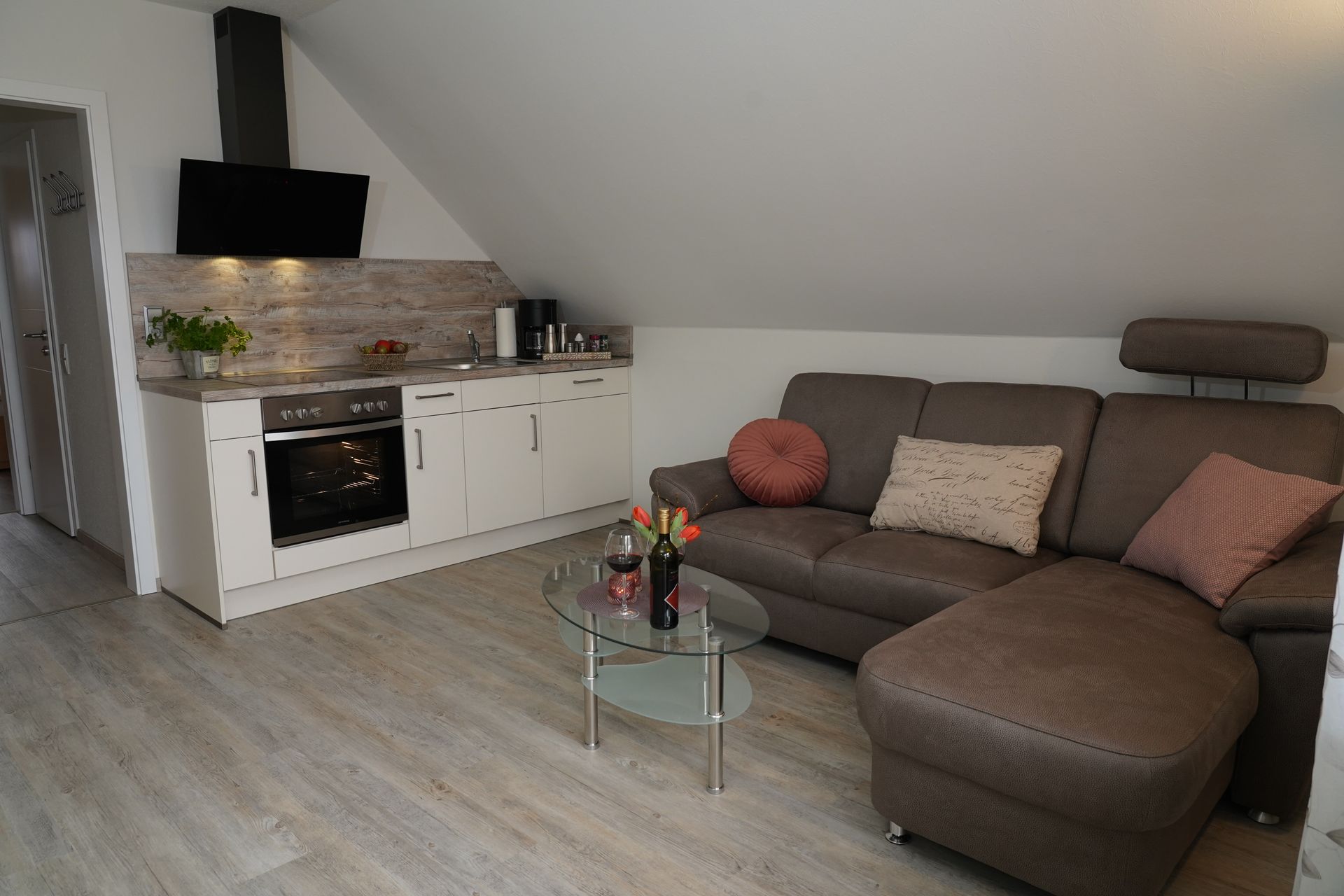 Modernes Dachgeschosswohnzimmer mit grauem Ecksofa, Glas-Couchtisch und weißer Küchenzeile