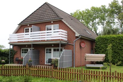Backsteinhaus mit weißem Balkon, Vorgarten und Holzzaun in einem grünen Hof