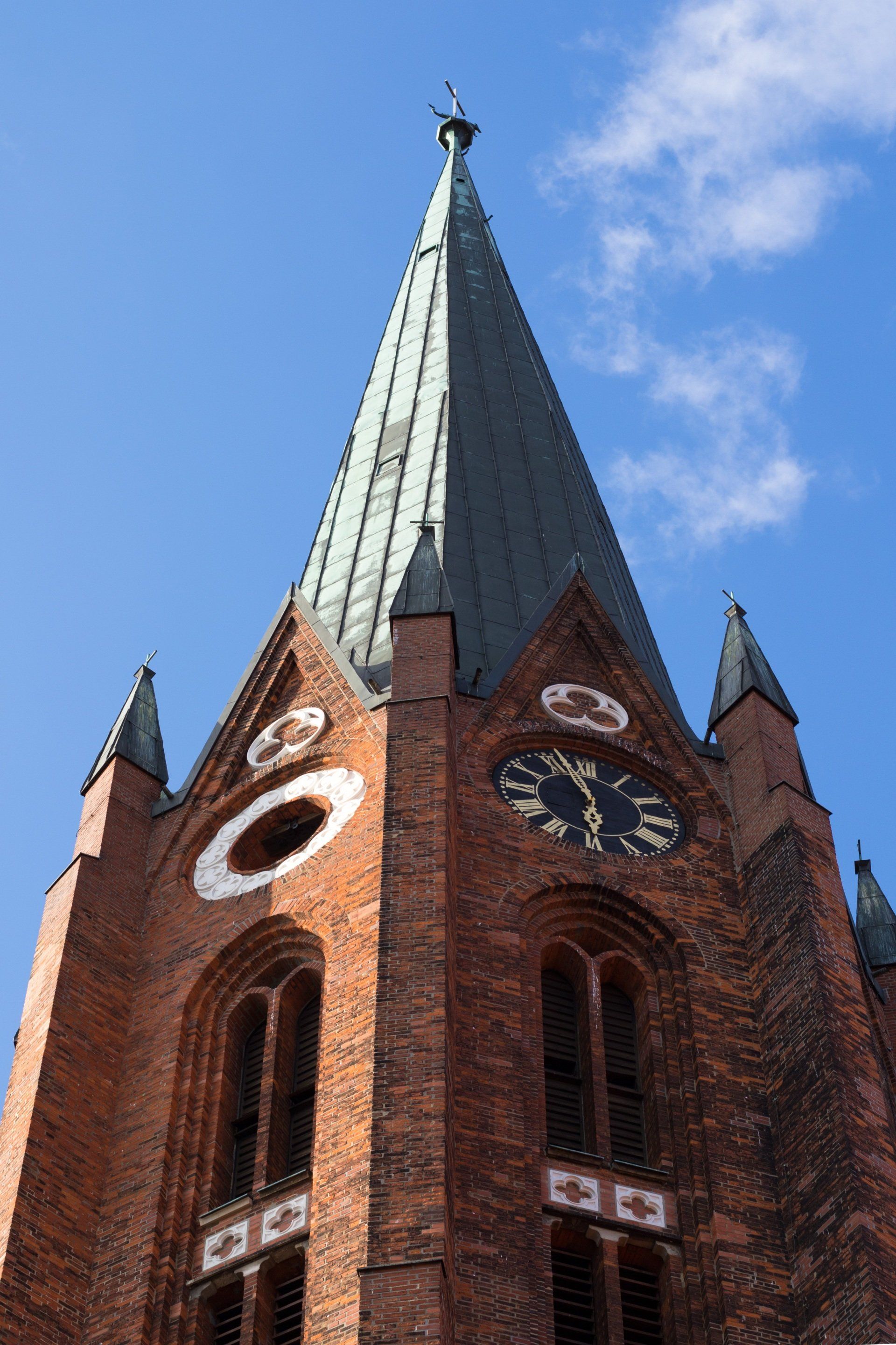 Backsteinkirchenturm mit grüner Spitze vor blauem Himmel