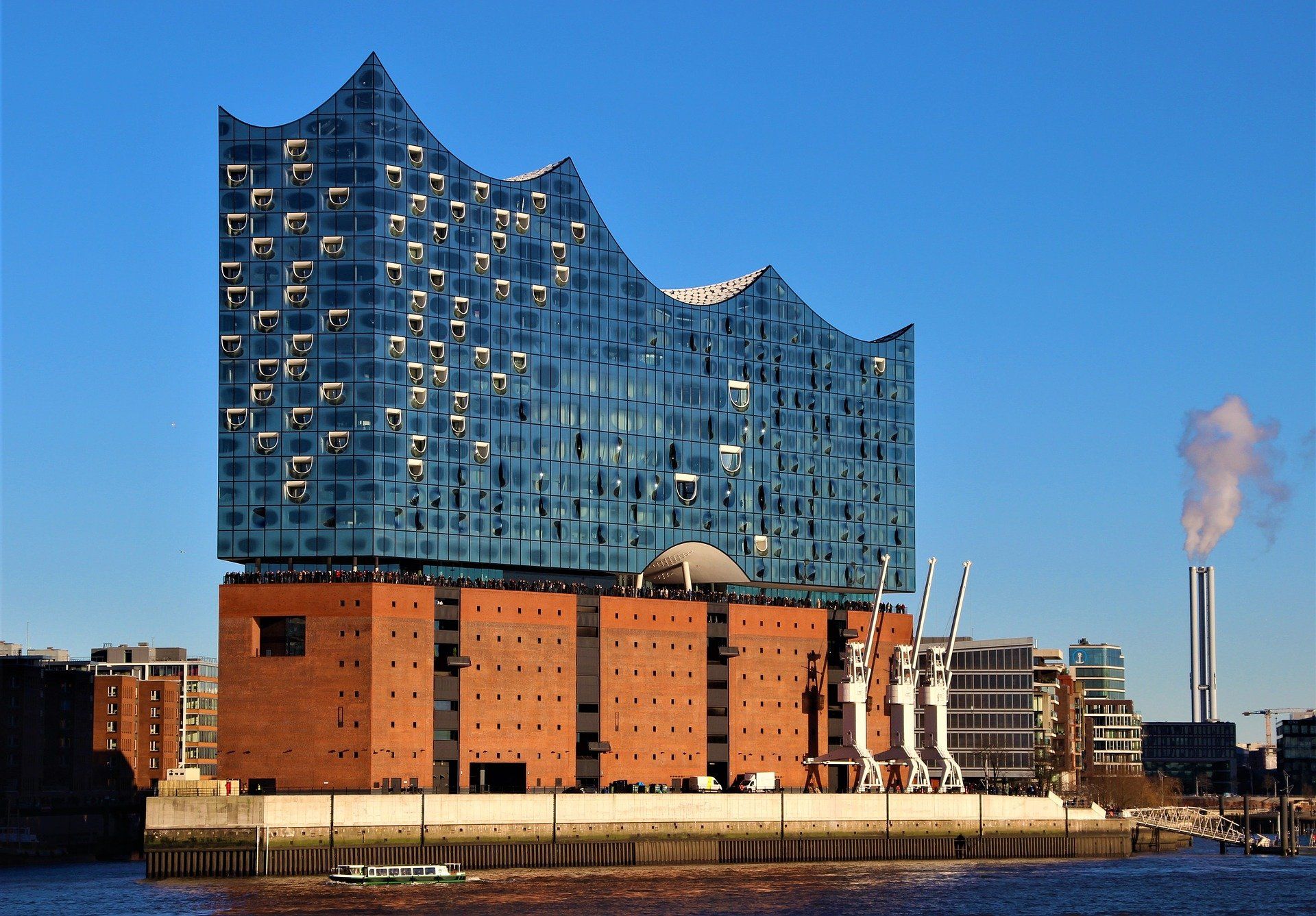 Die Hamburger Elbphilharmonie mit ihrer geschwungenen Glasfassade am Wasser bei Sonnenuntergang