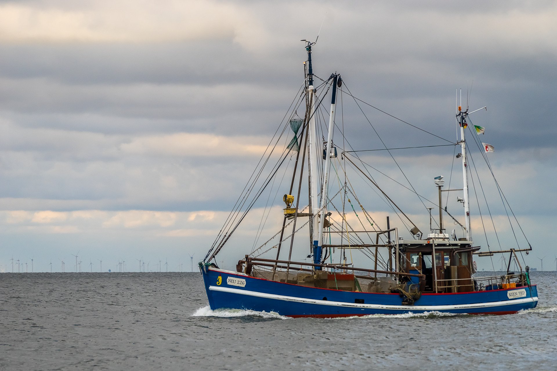 Blaues Fischerboot auf ruhigem Wasser unter bewölktem Himmel
