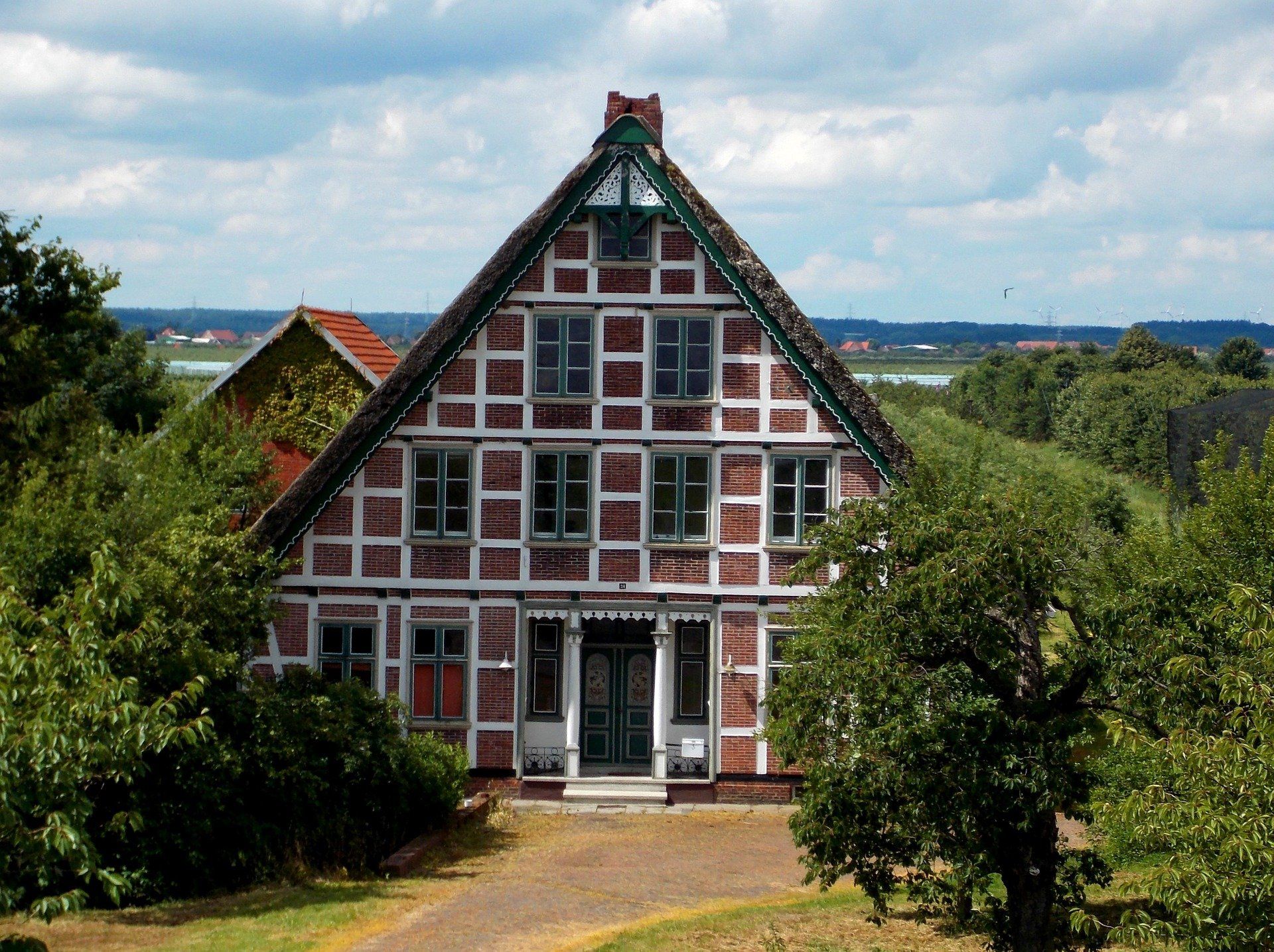 Ein historisches Fachwerkhaus mit rotem Zierwerk, durch Bäume unter einem bewölkten Himmel zu sehen.