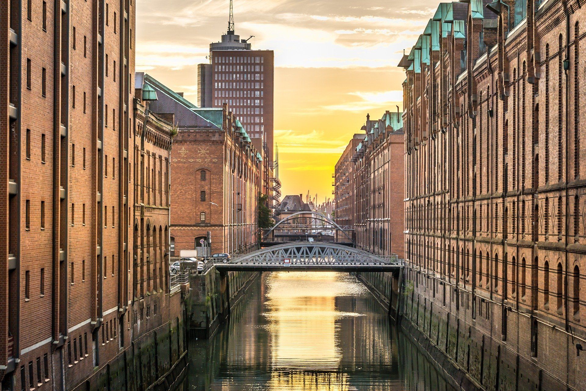 Kanal zwischen Backsteingebäuden der Speicherstadt bei Sonnenuntergang mit einer Brücke und Spiegelungen im Wasser
