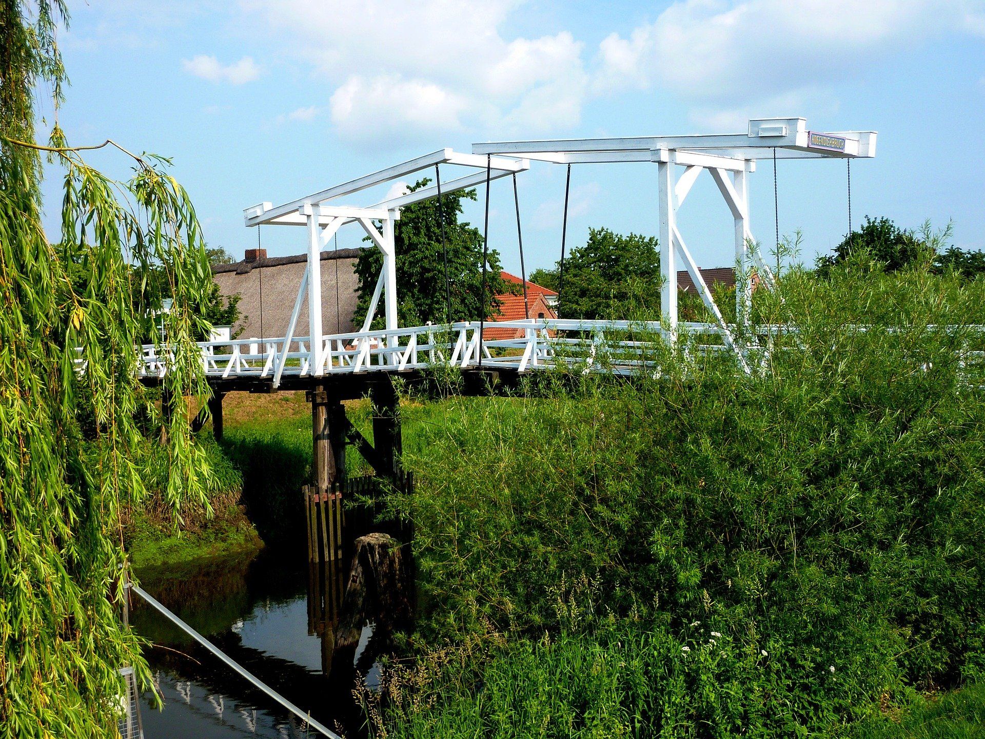 Die Hogendiek-Brücke über die Lühe, umgeben von üppig grünen Bäumen und Sträuchern unter klarem Himmel