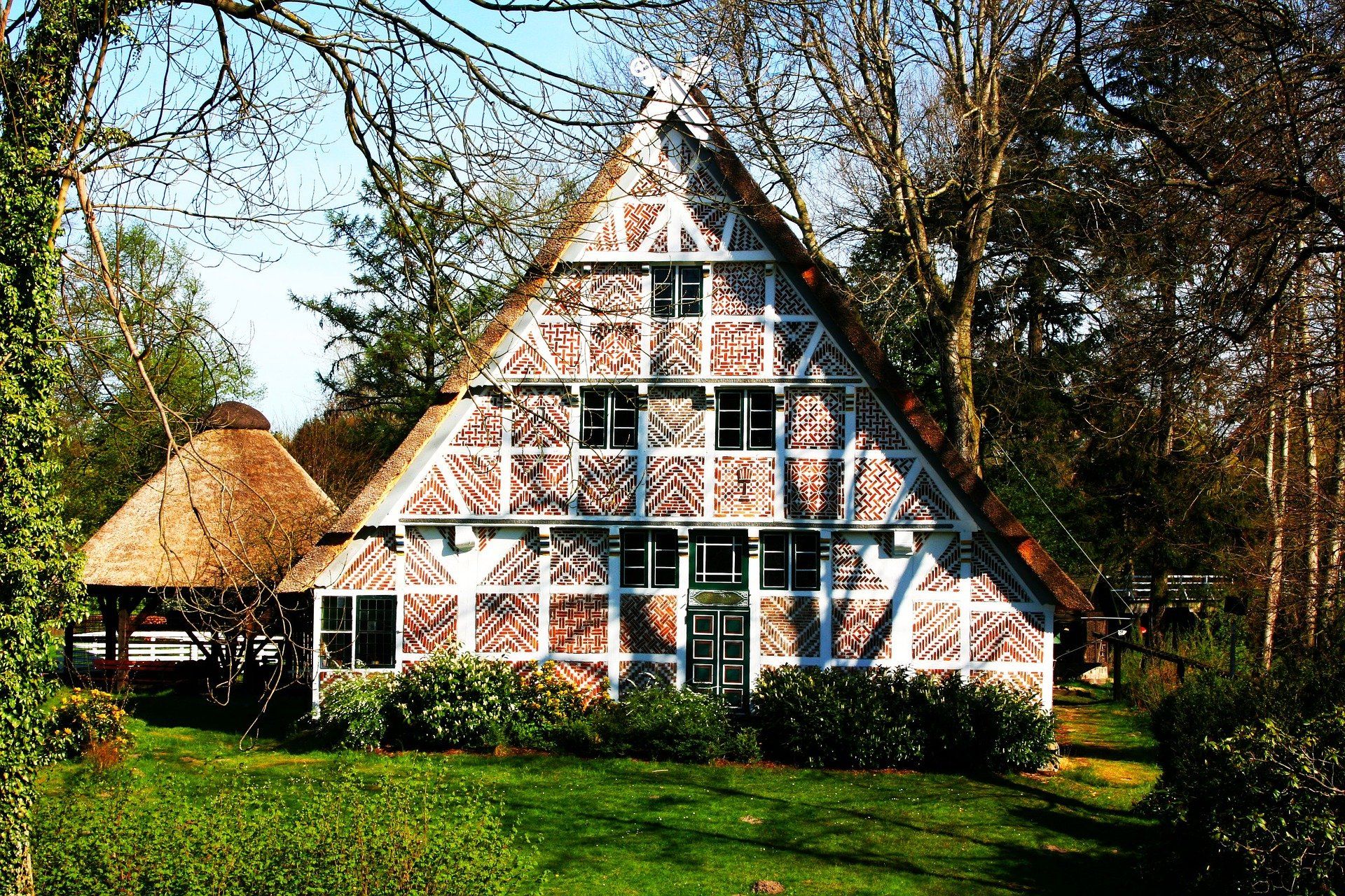 Reetgedecktes Häuschen mit rot-weißem Fachwerk in einem grünen Garten unter Bäumen