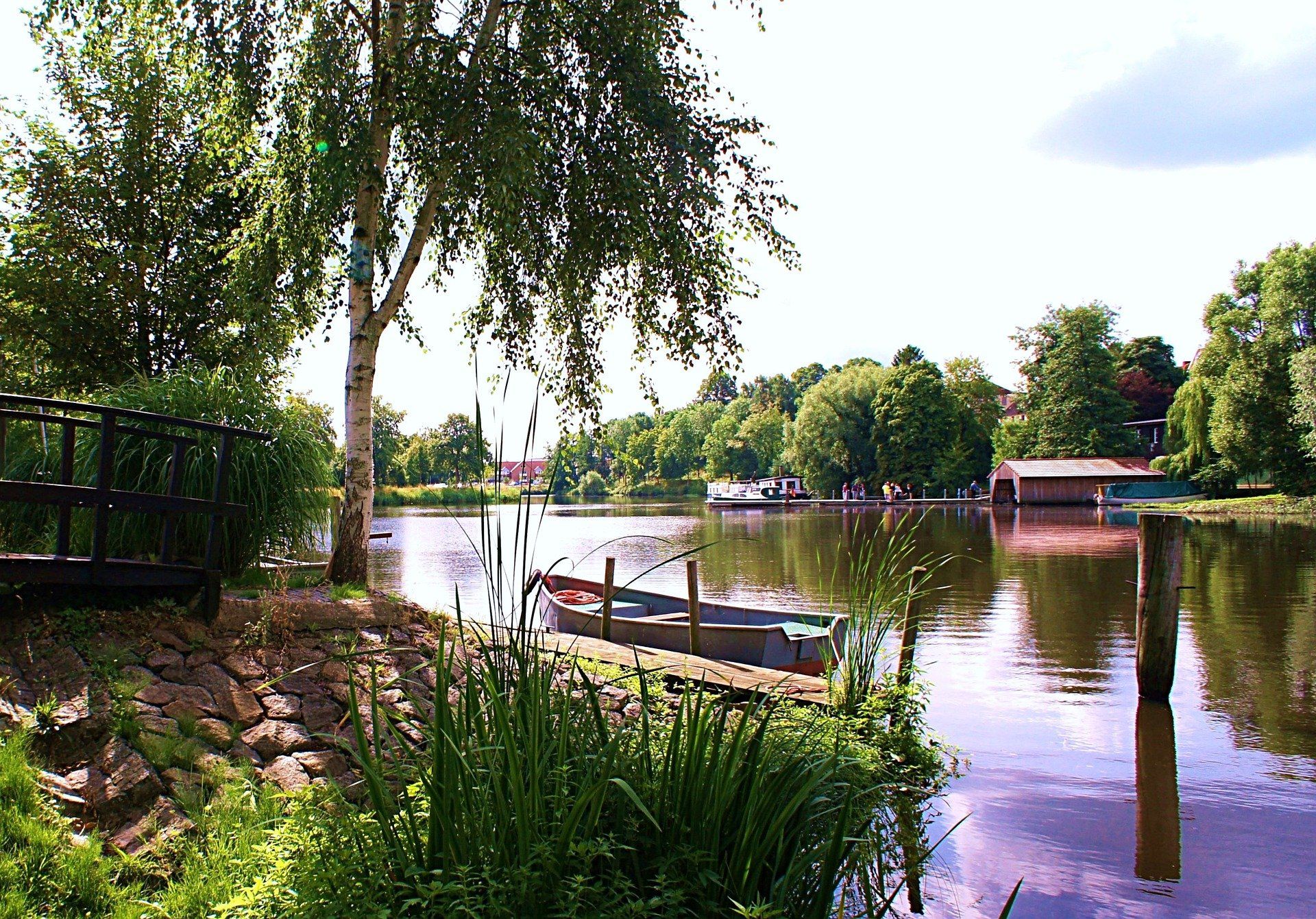 Friedliche Szene am Burggraben mit einem Steg, einem kleinen Boot, Bäumen und Spiegelungen im ruhigen Wasser