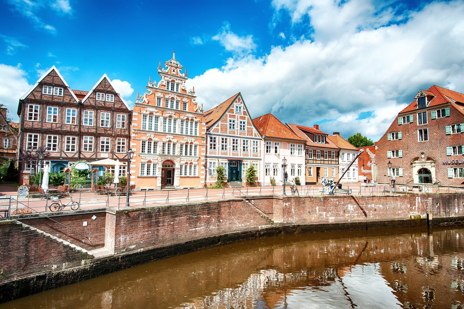 Farbenfrohe, historische Gebäude am Kanalufer mit roten Dächern spiegeln sich im ruhigen Wasser unter einem hellen Himmel